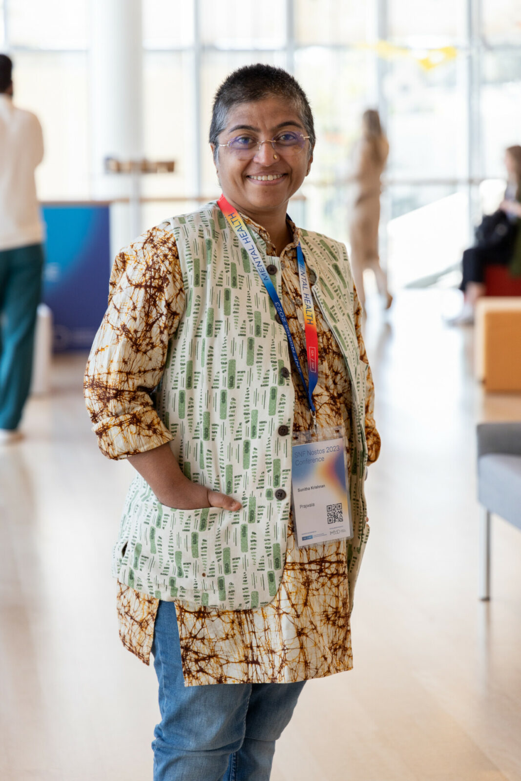 Sunitha Krishnan stands in a bright hall. She smiles at the camera, has her colored conference badge around her neck and her hands in the pockets of her green vest.