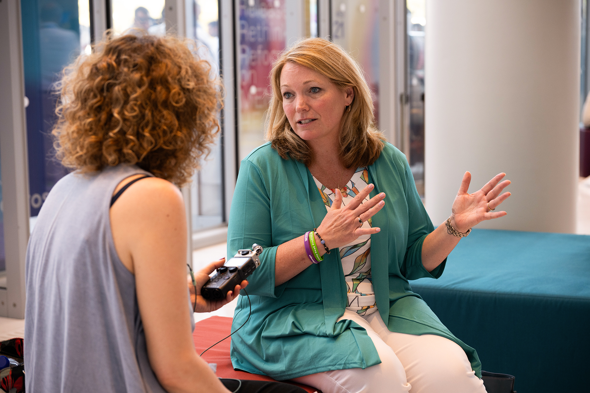 Nicole Hockley speaking with reporter at SNF Nostos. She looks straight at the reporter who holds a recording device.