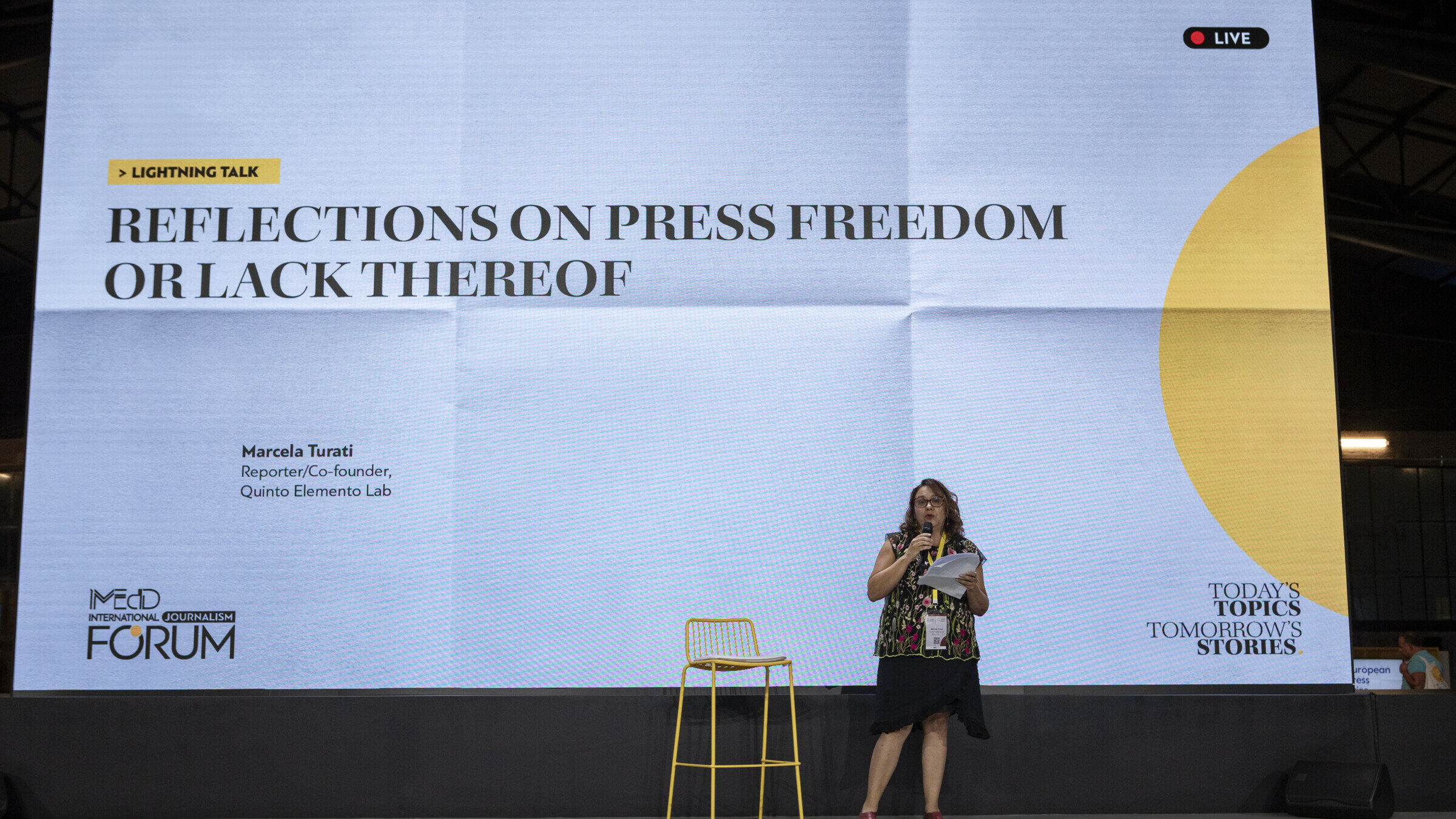 Η Marcela Turati κρατά το μικρόφωνο και ένα κομμάτι χαρτί ενώ στέκεται στην κεντρική σκηνή του Διεθνούς Φόρουμ Δημοσιογραφίας του iMEdD. Παρουσιάζει στην σειρά ομιλιών με τίτλο «Σκέψεις για την ελευθερία του Τύπου ή την έλλειψη της». Πίσω της, μια μεγάλη οθόνη με τον τίτλο της σειράς ομιλιών, καθώς και το όνομα και τον ρόλο της Marcela Turati ως ρεπόρτερ και συνιδρύτρια του Quinto Elemento Lab.
Λεζάντα: Φωτογραφία: Χρήστος Καραγεωργάκης
