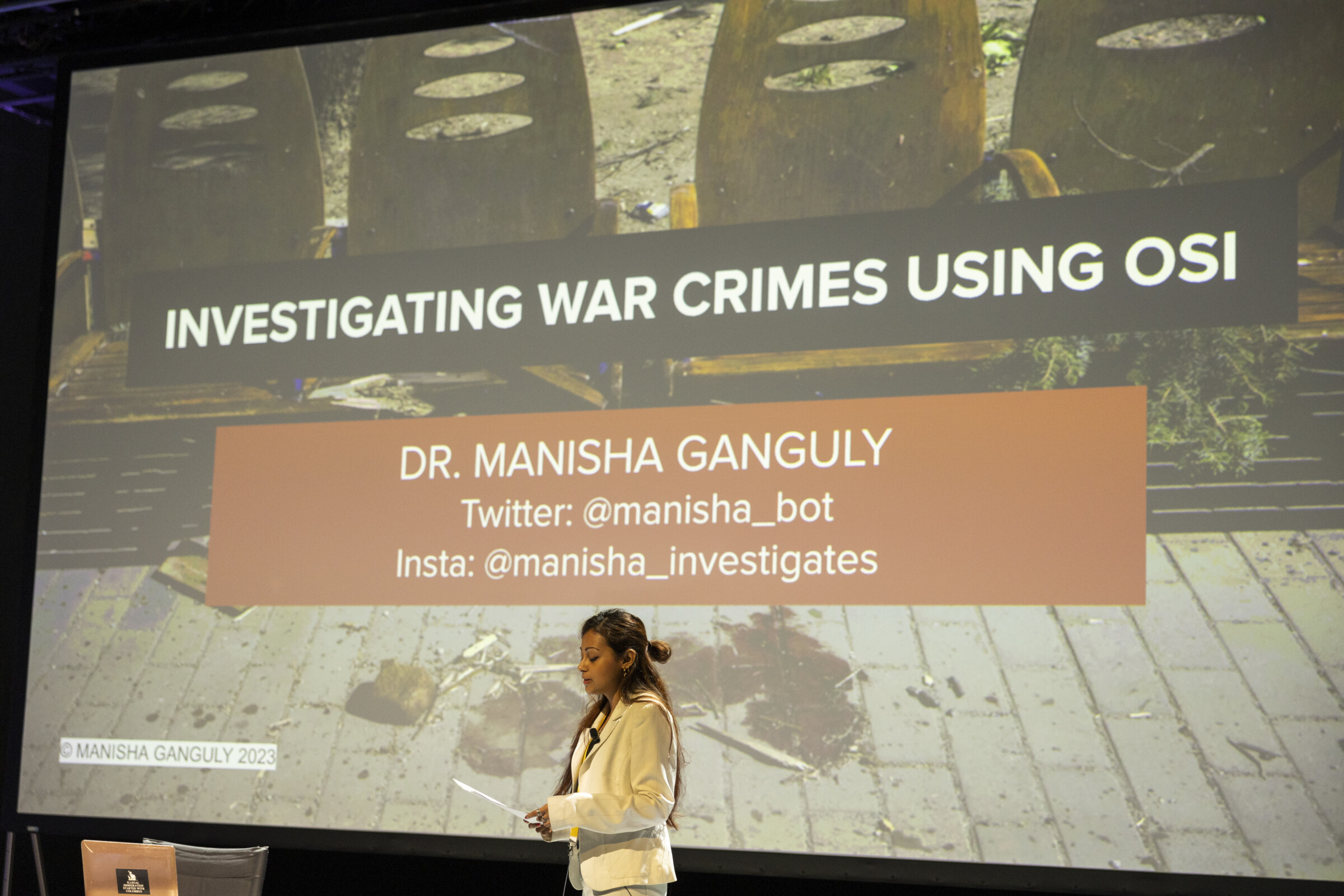This photo shows Manisha Ganguly during the presentation of her workshop "Investigating war crimes using OSINT", in the framework of the iMEdD International Journalism Forum. On the back is a slide with the title of the workshop and Manisha Ganguli's name and contact details.