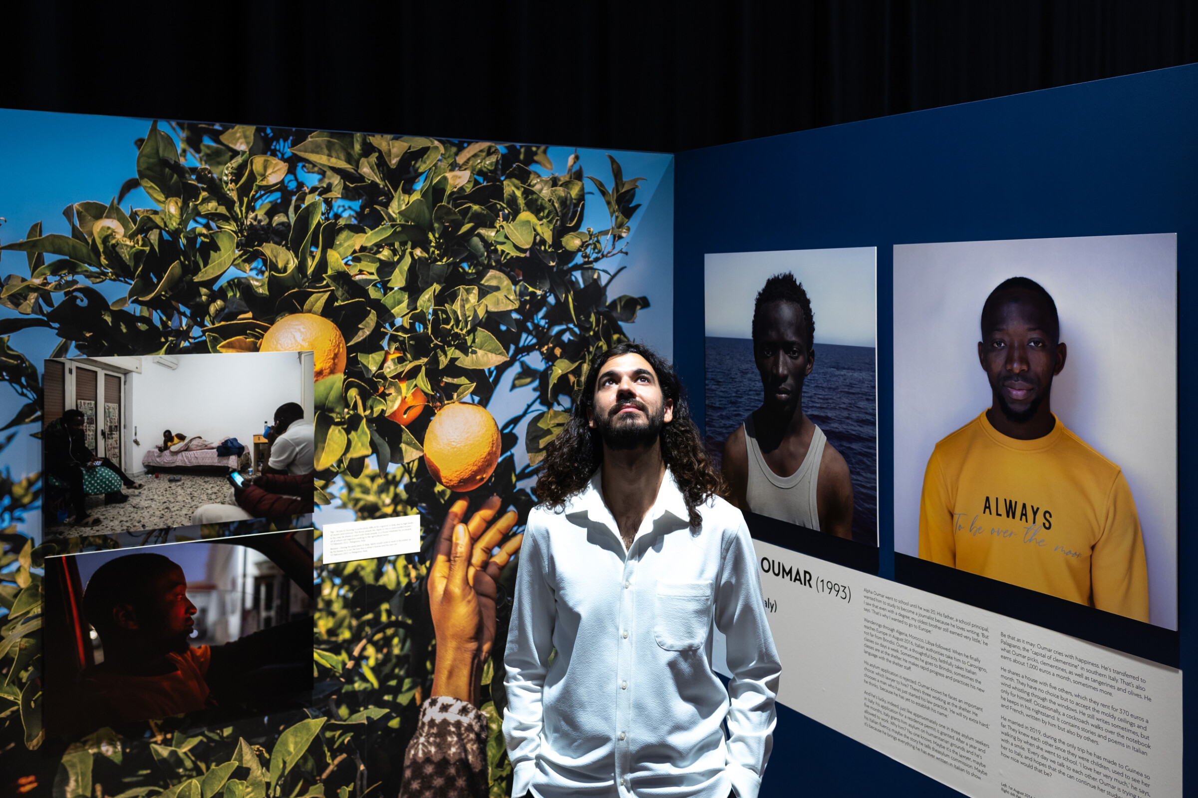 This image, taken in the context of the iMEdD International Journalism Forum, shows Spanish-Iranian photojournalist Cesar Dezfuli posing among the images of his photo exhibition project entitled "Passengers".