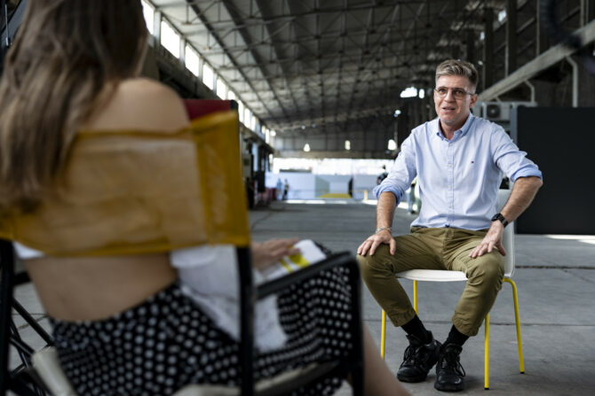 Paul Radu sits on a chair at the entrance of the venue, where the iMEdD 2024 International Journalism Forum took place, looking at the interviewer. Radu is in focus while the interviewer is out of focus and has their back on the camera.